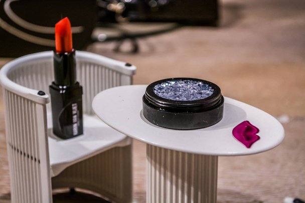 Small white table and chairs. Cosmetics. Red lipstick and eye shadow with spangles. - Foto, afbeelding