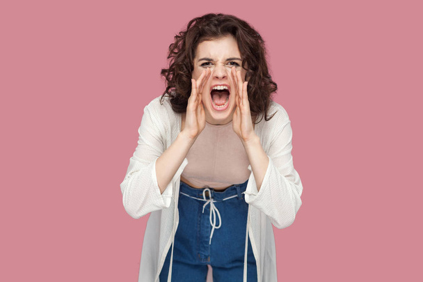beautiful brunette young woman with curly hairstyle in casual style looking at camera and screaming on pink background - Photo, Image