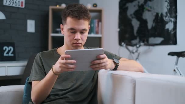 Round close-up view of a handsome teenager surfing the web on his tablet at home - Video