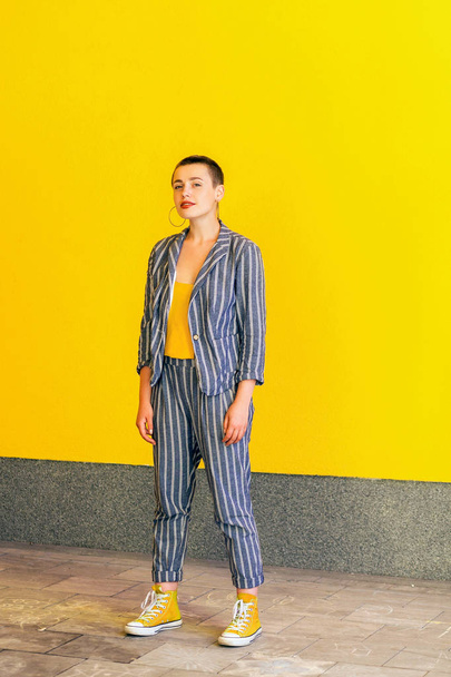 happy satisfied young short hair beautiful woman in casual yellow shirt and striped suit standing and looking at camera with toothy smile on yellow background. - Fotoğraf, Görsel