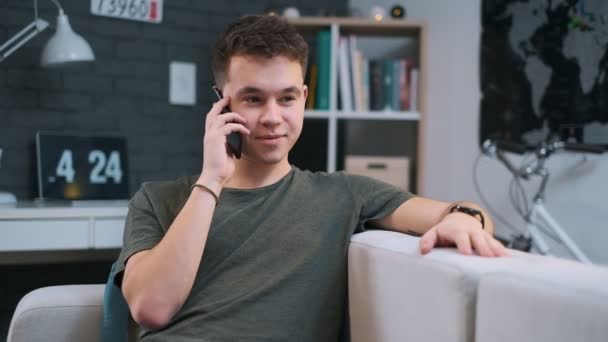 Close-up view of a handsome teenager talking on the phone while resting on the couch in his room - Imágenes, Vídeo