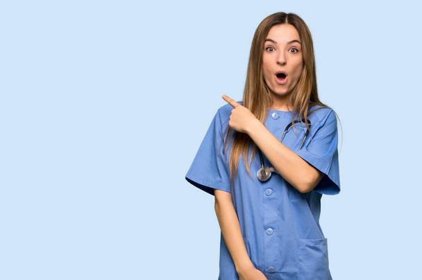 Young nurse surprised and pointing side on isolated blue background - Φωτογραφία, εικόνα