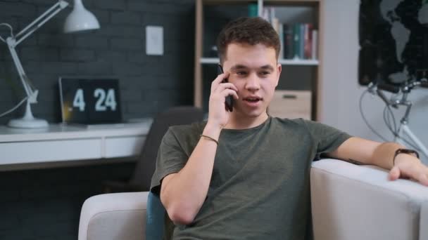 Close-up portrait of a sweet stylish teenage boy talking on the phone at home - Filmati, video