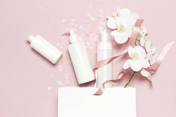 Düz üst görünüm Beyaz kozmetik şişe kapları şenlikli konfeti hediye çantası Beyaz Phalaenopsis orkide çiçekler pembe arka plan üzerinde yatıyordu. Kozmetik Spa markamake-up Doğal organik güzellik ürünü - Fotoğraf, Görsel