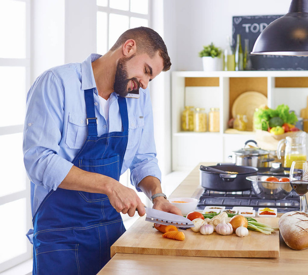 Ο νεαρός σεφ ετοιμάζει έναν άντρα στην κουζίνα. - Φωτογραφία, εικόνα