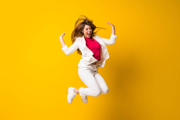 Young woman jumping over isolated yellow wall - Фото, зображення