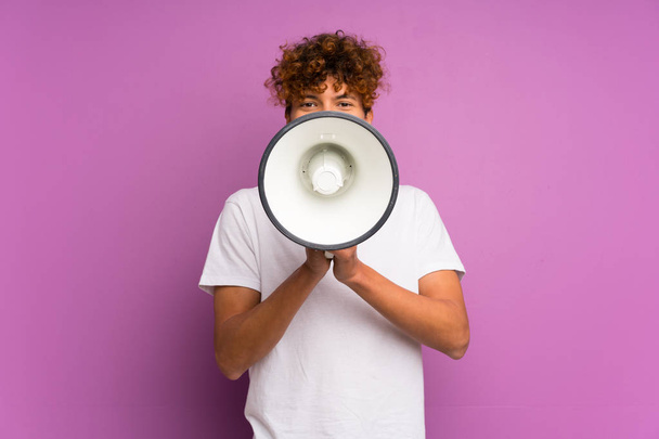 Молодий афроамериканець над ізольованою фіолетовою стіною кричить через мегафон. - Фото, зображення