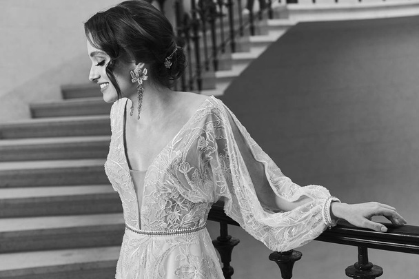 Cinematic portrait of emotional and beautiful brunette bride in luxury dress standing on stairs. Black and white - Fotoğraf, Görsel