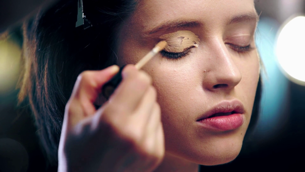 vista parcial del maquillador aplicando corrector sobre el párpado modelo con pincel cosmético
 - Metraje, vídeo