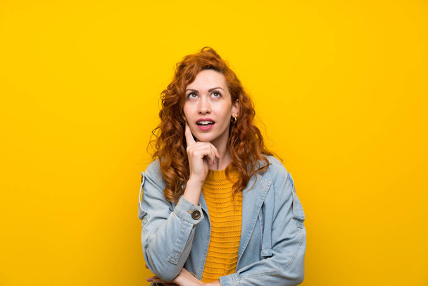 Redhead woman over isolated yellow background thinking an idea - Foto, afbeelding