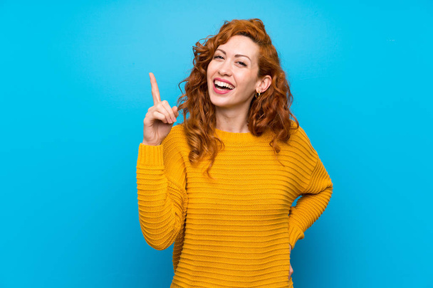 Redhead woman with yellow sweater intending to realizes the solution while lifting a finger up - Photo, image