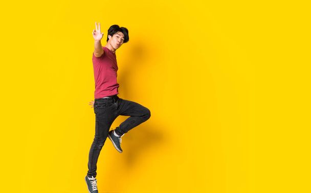 Asian man jumping over isolated yellow wall - 写真・画像