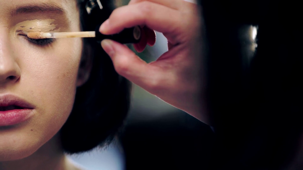 cropped view of makeup artist applying concealer on model eyelid with cosmetic brush - Footage, Video