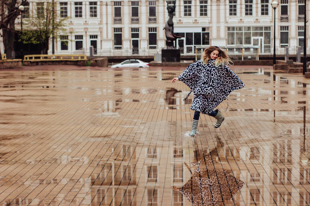 Stylische Frau in Regenmantel und Gummistiefeln spaziert durch die Pfützen und hat Spaß - Foto, Bild