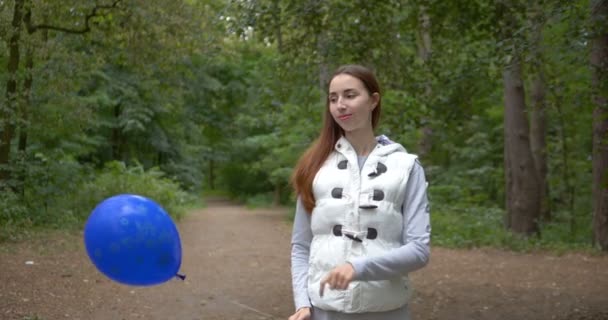Chica feliz de pie con un globo azul y sonriendo en un bosque en slo-mo
 - Metraje, vídeo