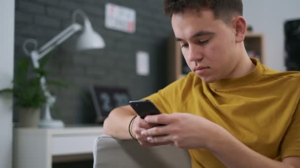 Close-up video of a teenager typing something on his smartphone, stylish room on a background - Felvétel, videó