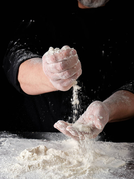 chef in black uniform sifts through his fingers white wheat flou - Foto, Bild