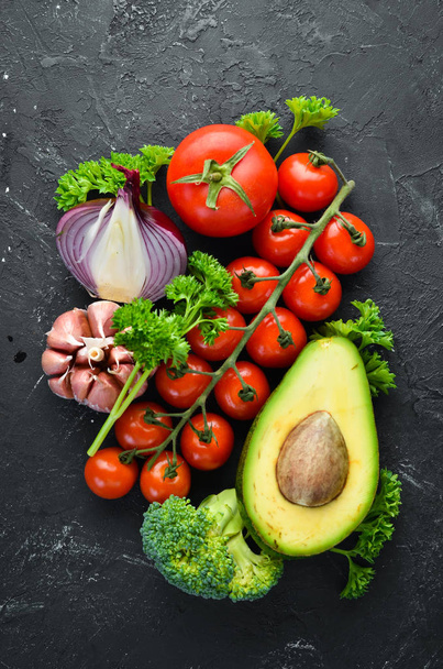 Fresh vegetables on a black background. Avocados, tomatoes, garlic, parsley, paprika. Top view. Free space for your text. - Photo, Image