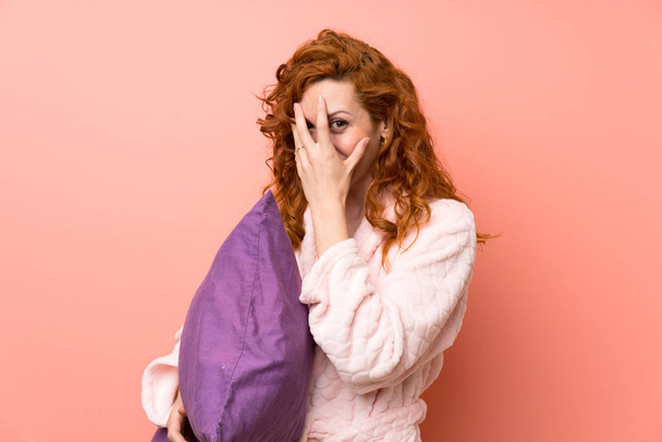 Redhead woman in dressing gown covering eyes and looking through fingers - Foto, imagen