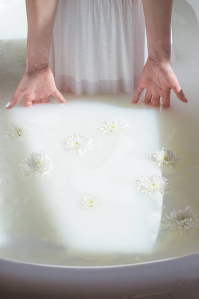 photo women's dress and hands dropped in a natural milk bath with foam and flowers - Фото, зображення