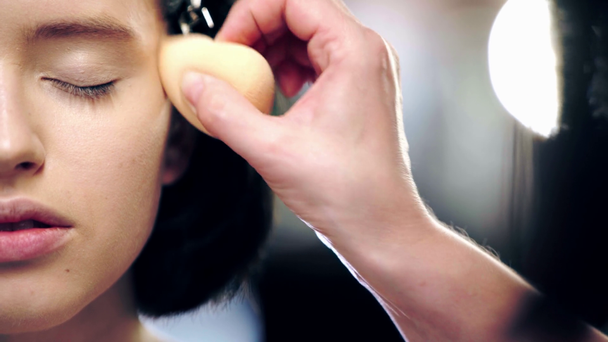 Ausgeschnittene Ansicht der Visagistin, die Concealer mit Kosmetikschwamm auf das Modell-Augenlid aufträgt - Filmmaterial, Video