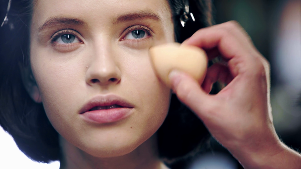 vista recortada de artista de maquillaje aplicando corrector bajo ojo modelo con esponja cosmética
 - Imágenes, Vídeo