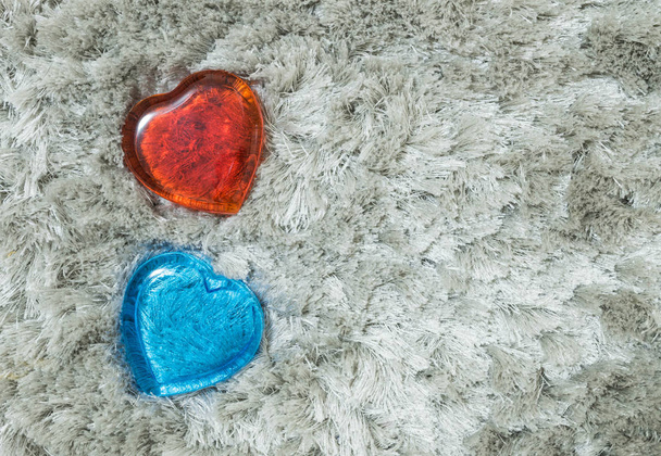 Primer plano de vidrio rojo y azul en forma de corazón sobre fondo texturizado alfombra gris
 - Foto, imagen