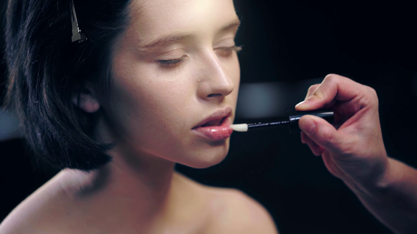 partial view of makeup artist applying shiny lip gloss on model lips with cosmetic brush - Materiaali, video