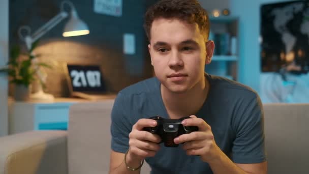Teenage boy playing a video game with a controller on the couch, getting disappointed in the end because he lost - Video, Çekim