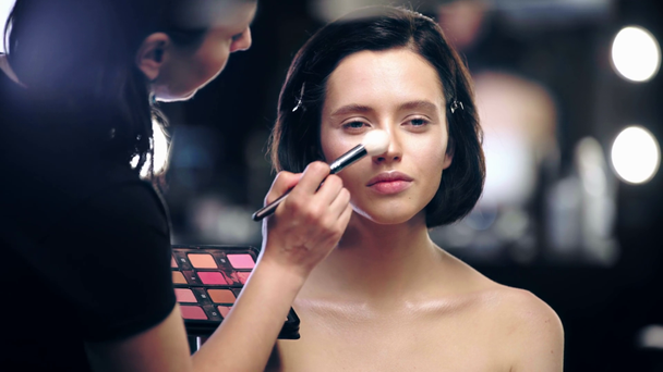 artista de maquiagem segurando paleta de cosméticos e aplicando iluminador no rosto modelo
 - Filmagem, Vídeo
