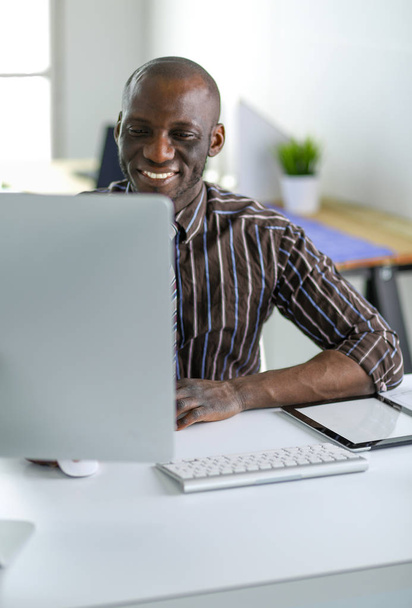 Przystojny Afro amerykański biznesmen w klasyczny garnitur jest za pomocą laptopa i uśmiechając się podczas pracy w biurze - Zdjęcie, obraz