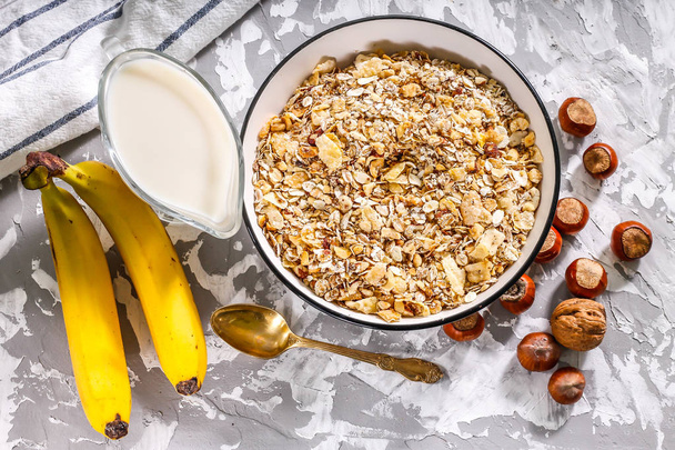 Muesli con nueces en un tazón con plátanos y leche sobre un fondo de hormigón - desayuno seco
. - Foto, Imagen