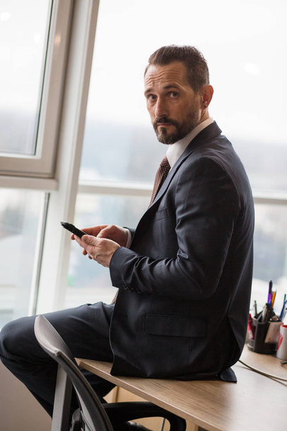 Handsome Businessman Sitting On Desk In Office - Foto, afbeelding