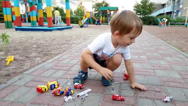 4k záběry 3 let starého batole hocha, který sedí na zemi na hřišti a hraje si s hračkářama - Záběry, video