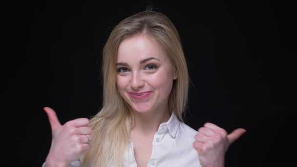 Joyful young businesswoman in white shirt gives a thumb-up to show like and respect on black background. - Footage, Video