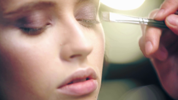 vista de cerca del artista de maquillaje sombreado sombra de ojos marrón en el párpado modelo con cepillo cosmético
 - Metraje, vídeo