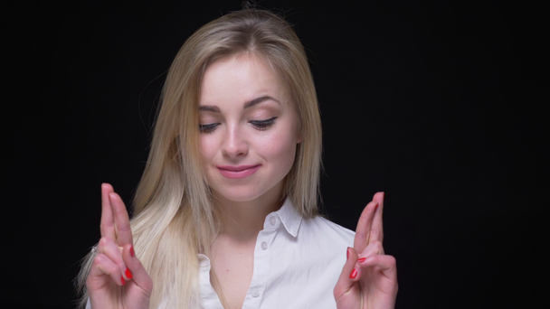 Joyful young businesswoman in white shirt praying with crossed fingers on black background. - Footage, Video