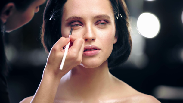 vista recortada del artista de maquillaje aplicando sombra de ojos en el párpado inferior modelo con cepillo cosmético
 - Metraje, vídeo