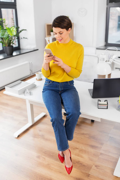 happy woman with smarthone sitting on office desk - Foto, Bild