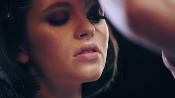 close up view of makeup artist applying mascara on eyelashes isolated on black - Video, Çekim