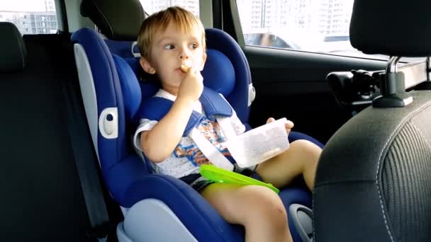 4k Filmmaterial von 3-jährigem Kleinkind, das im Kindersitz sitzt und isst - Filmmaterial, Video