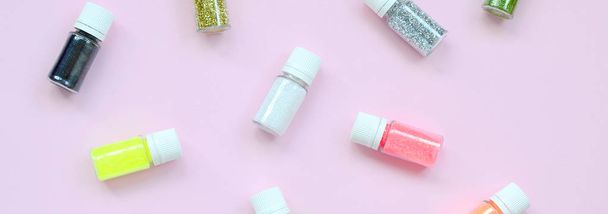 Een vlakke lay patroon met kleurrijke glitter flessen ligt op pastel roze achtergrond. Veel ronde potten met veelkleurige heldere sparkles voor nagellak. Sprankelende pailletten. Top View - Foto, afbeelding