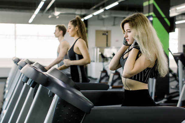 Young people running on a treadmill in health club. Girl running on the treadmill and listening to music at the gym - 写真・画像