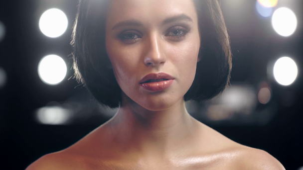 mooi naakt model met glanzende make-up kijkend naar de camera met bokeh-lampjes op de achtergrond - Video
