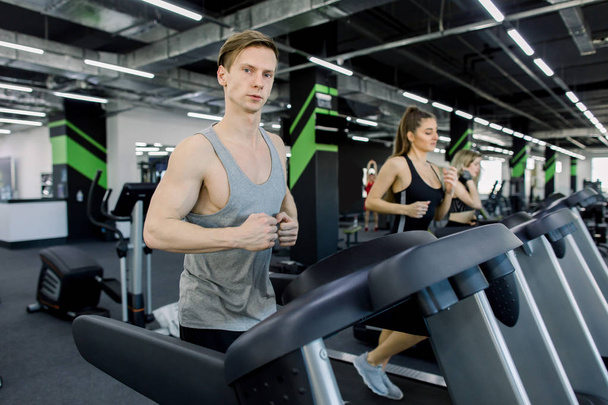 Picture of people running on treadmill in gym. Handsome trainer and two young women on the treadmill in gym. Fitness concept - Foto, Imagen