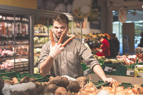 Man holding two carrots in a supermarket - Photo, Image