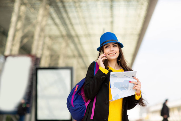 Красивая молодая девушка в рюкзаке и синей шляпе, разговаривает на мобильном телефоне на улице рядом с аэропортом
 - Фото, изображение