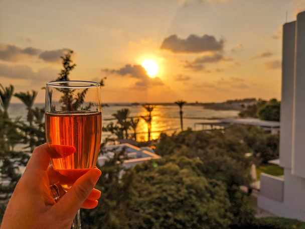Žena drží sklenici růžového šumivého vína s výhledem na záliv - Fotografie, Obrázek