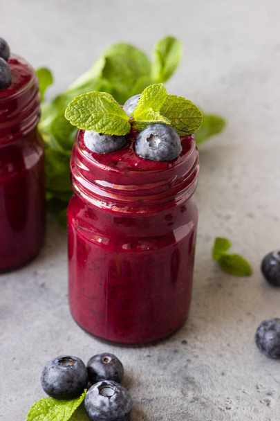 Delicious blueberry smoothie with fresh berries and mint in glass jars. Summer healthy drink. Grey stone background. Copy space. - Zdjęcie, obraz