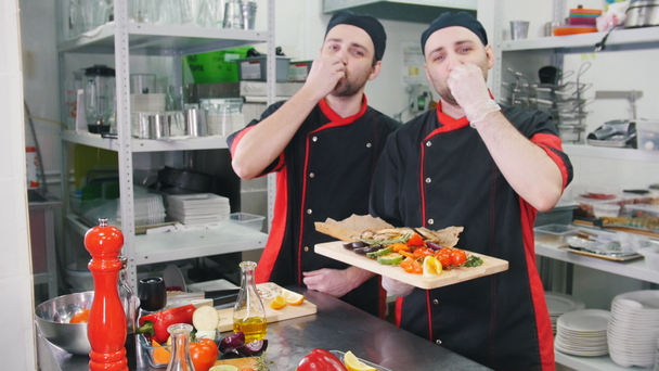 Restaurant kitchen. Two men chefs finished serving the dish, taking it on the hands and doing a bellissimo gesture - Footage, Video